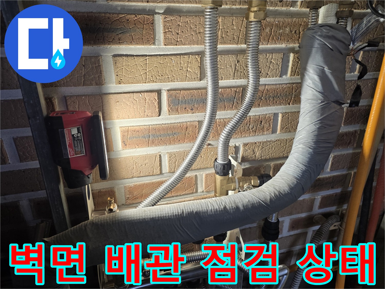 벽돌 벽면에 설치된 은색 주름관과 배관 연결 부위 모습