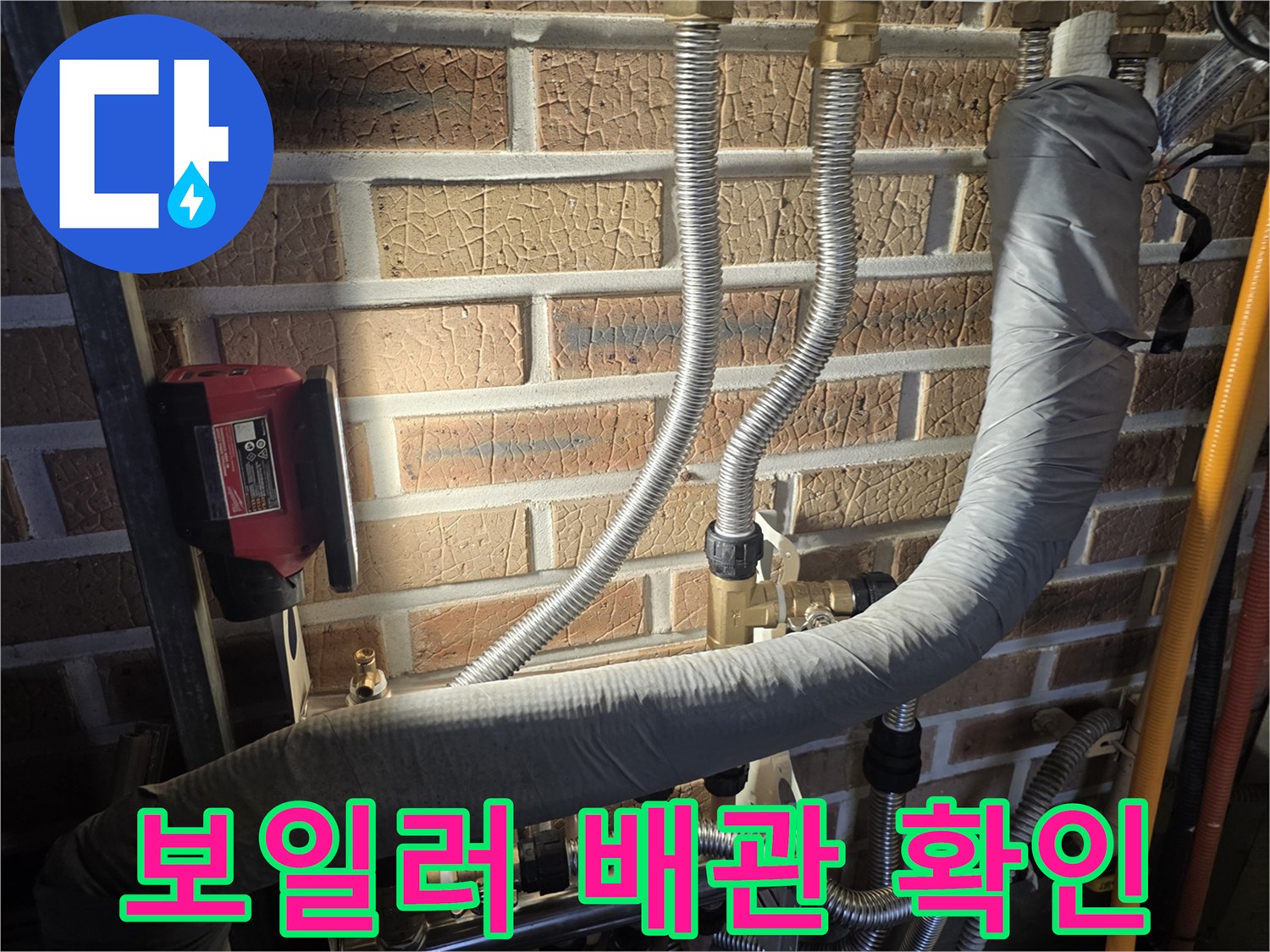 보온재로 감싸진 배관과 은색 연결 호스들이 벽면에 부착된 모습입니다.