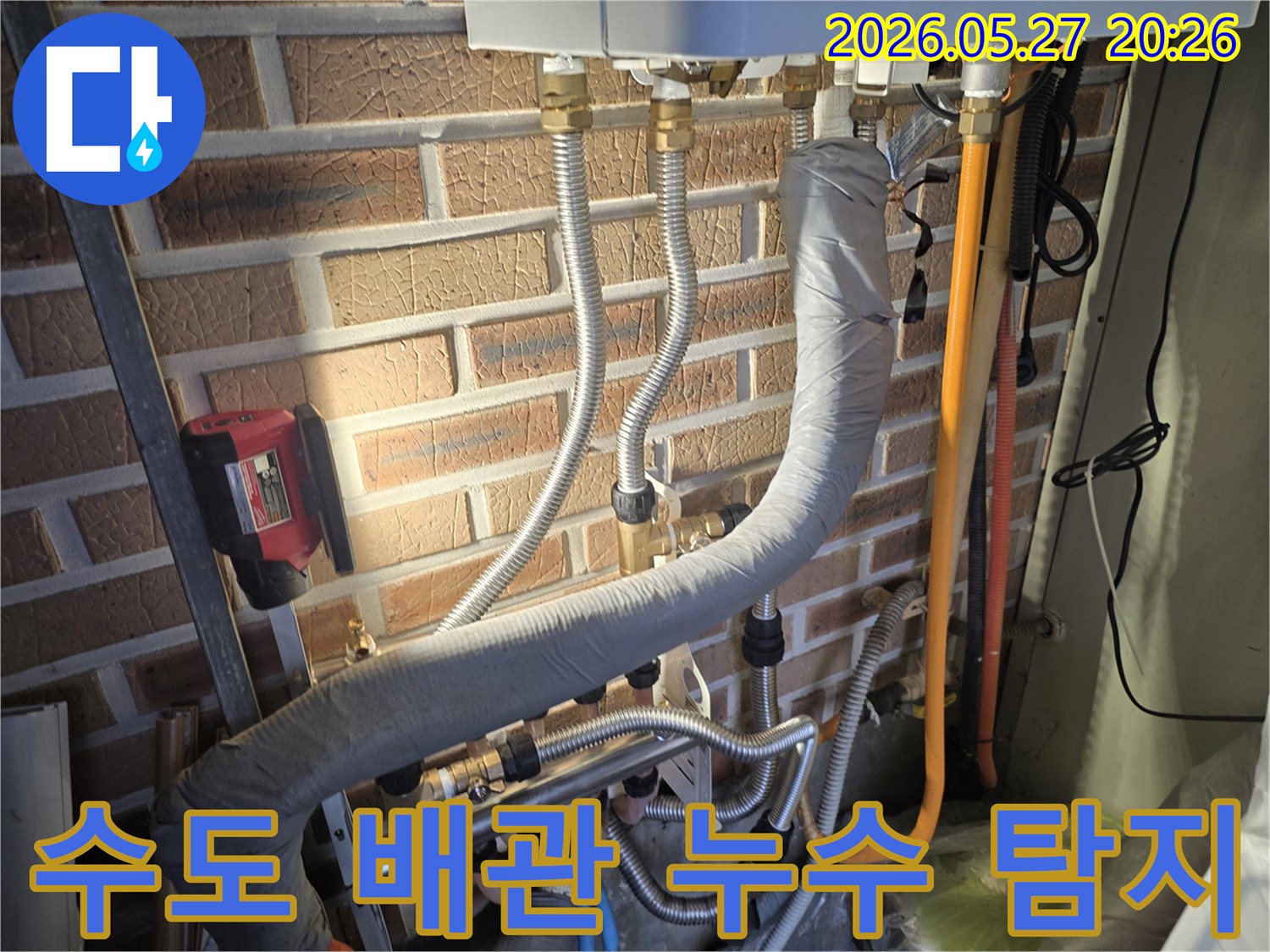 이 이미지는 벽돌 벽에 설치된 다양한 수도 배관과-연결 부위 그리고 누수 탐지를 위한 장비가 보이는 현장입니다.
