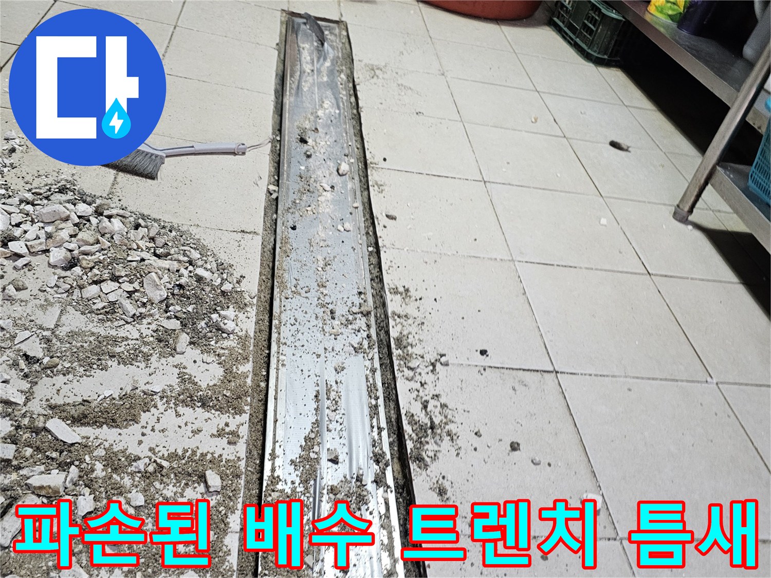 금속 소재의 긴 배수 트렌치와 주변에 흩어진 타일 파편