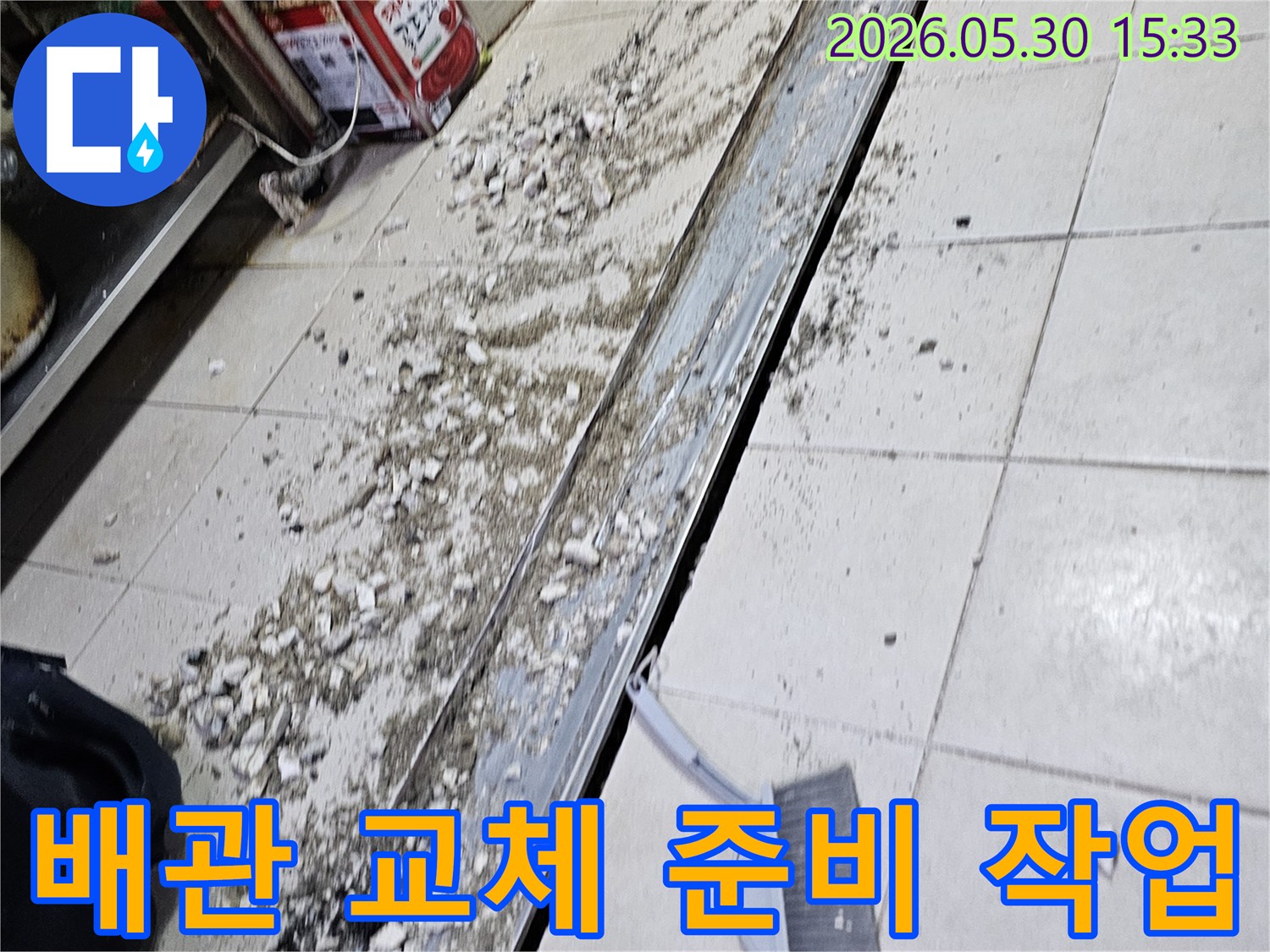 누수 공사 현장에서-바닥 타일 파쇄 후-발생한 잔해물과-청소 도구가-함께 보이는-작업 진행 모습입니다.