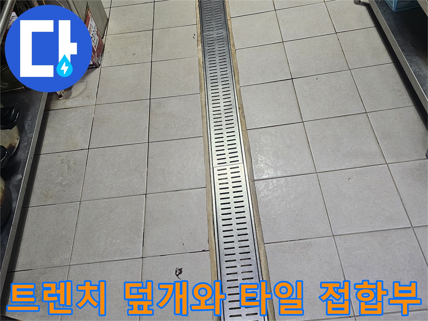 스테인리스 재질의 긴 배수 트렌치 구조물과 주변 바닥 타일