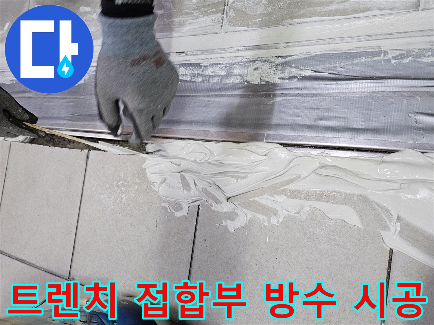 장갑을 낀 작업자가 트렌치와 타일 사이를 방수재로 메우는 사진