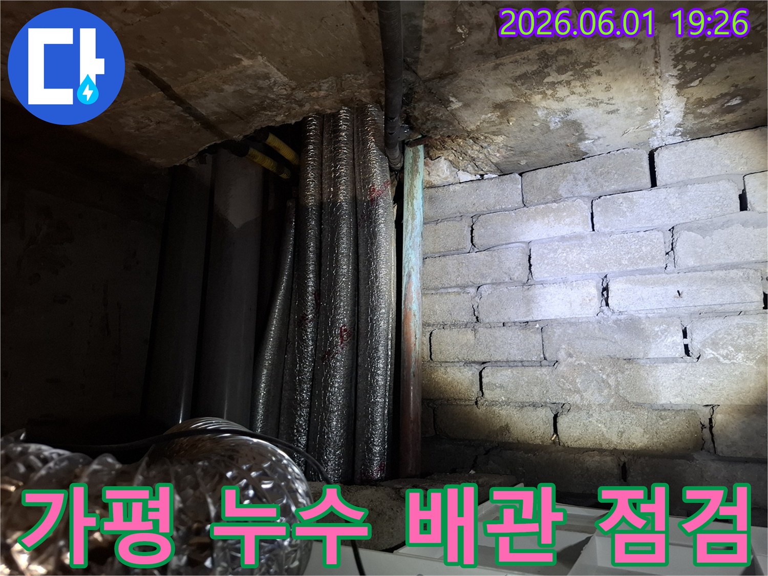 어두운 지하 공간에서-누수 흔적이 보이는-천장 배관과-벽돌 벽면의 모습입니다