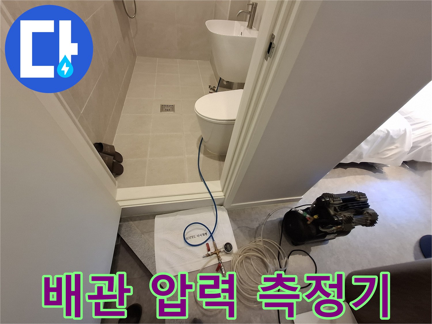 욕실 입구 바닥에 놓인 배관 압력 테스트용 게이지와 호스 연결 장치