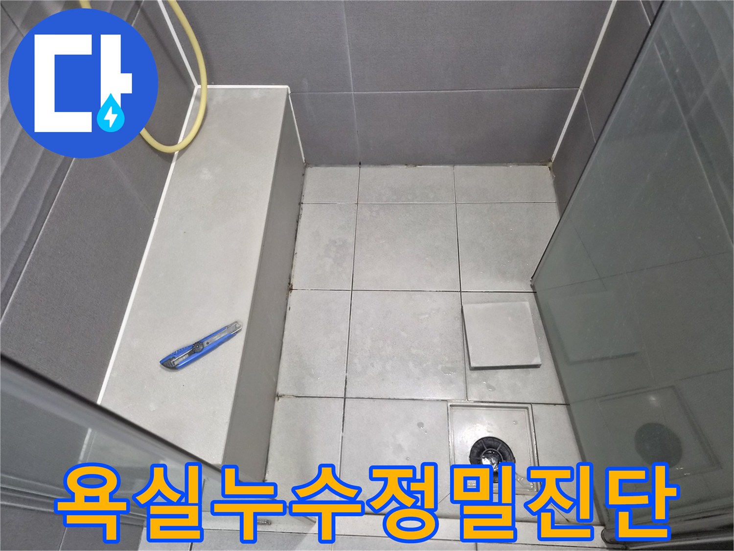 욕실-바닥-타일과-배수구-그리고-작업-도구인-커터칼이-놓여-있는-모습으로-누수-진단을-위한-현장-점검-사진입니다.