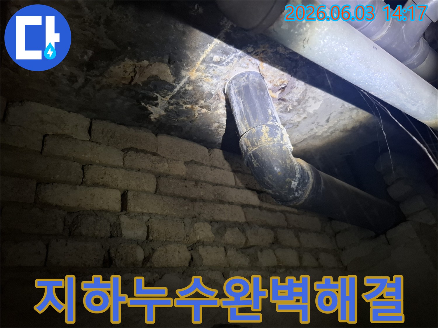 낡은 배관과-벽돌 벽이 있는-지하 공간에서-누수 발생 지점을-조명으로 비추며-세심하게 살펴보는 모습