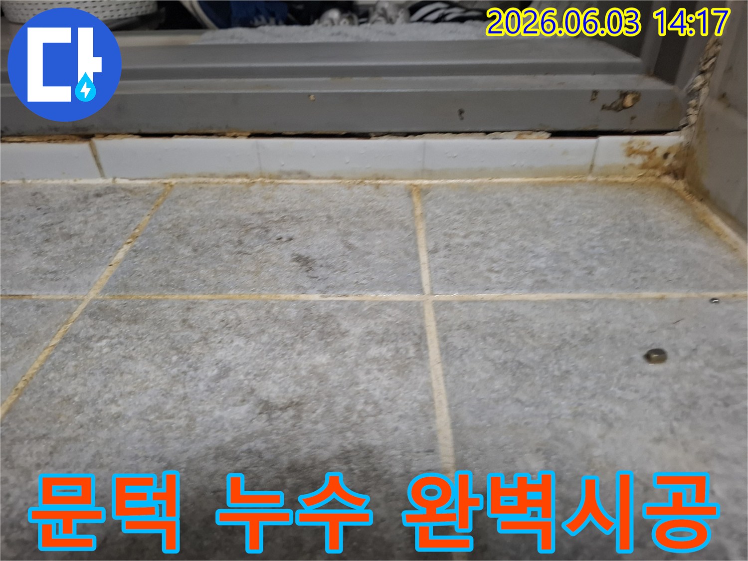 욕실 문턱 아래 타일 줄눈에 물이 스며들어-변색과 오염이 발생한 누수 흔적을 보여주는 이미지입니다.