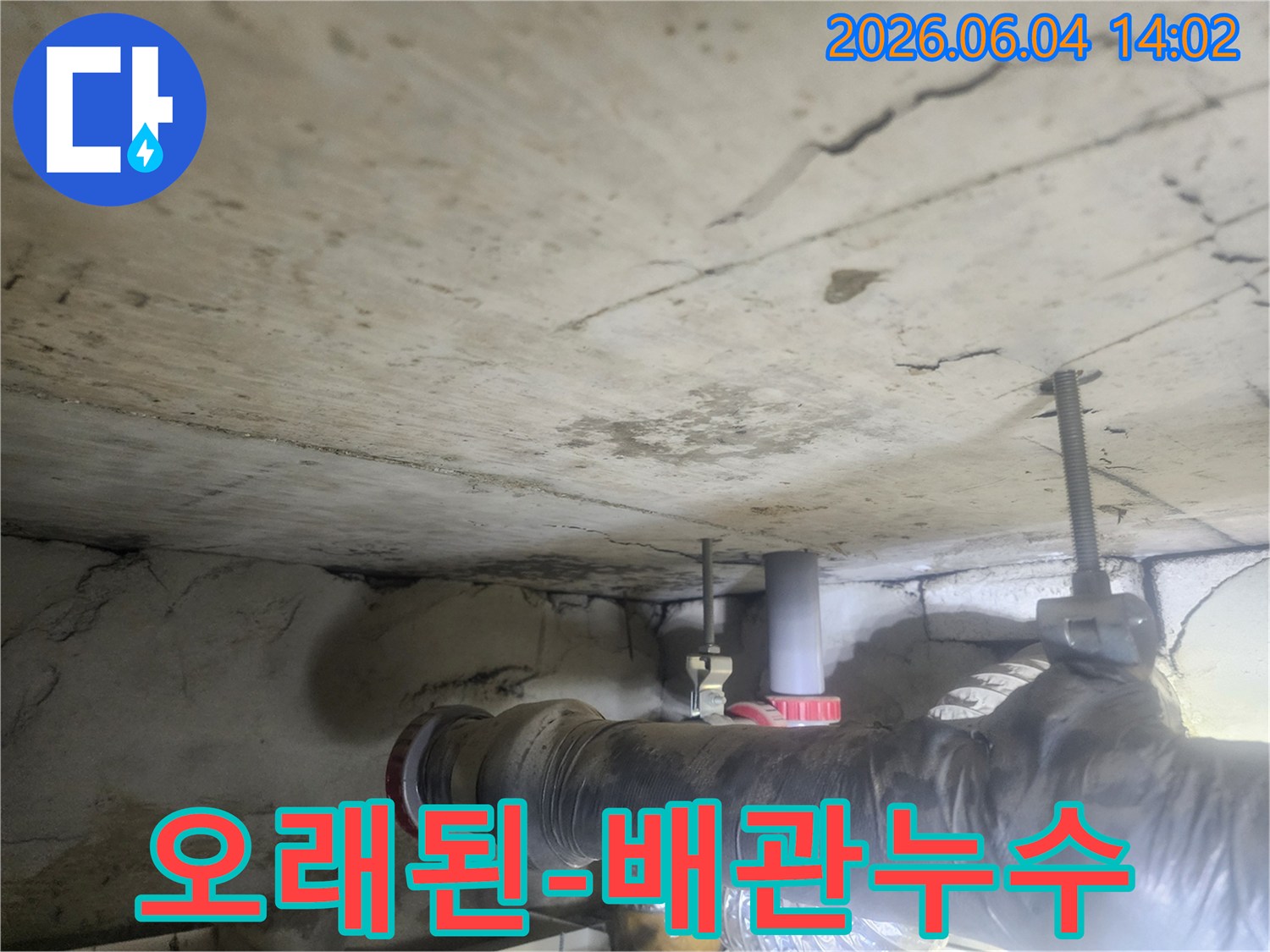 지하 천장의 낡은 배관과-그 주변으로 퍼진 물 자국은-누수 문제의 심각성을-드러냅니다.