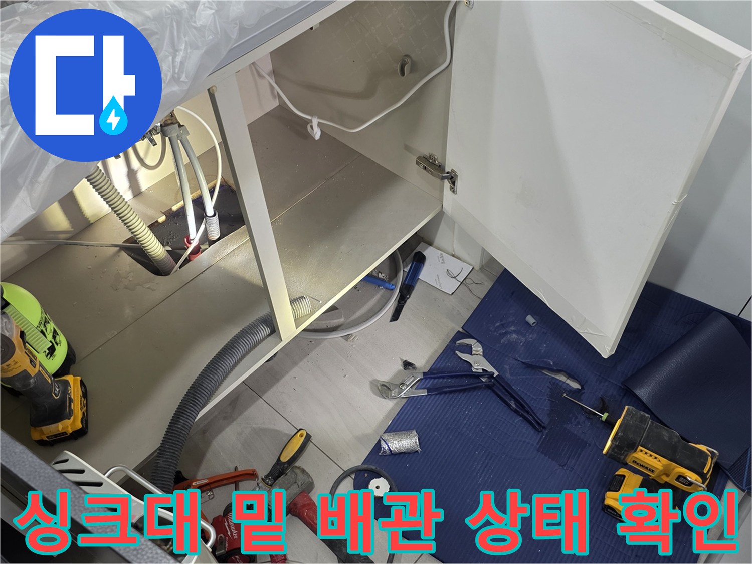 싱크대 하부의 배관 구조와 주변에 놓인 작업용 장비들