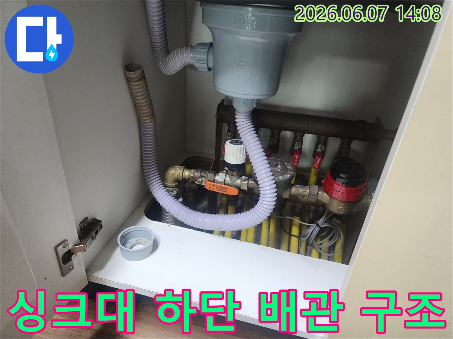 하얀색 싱크대 하부장 내부에 설치된 배수구와 급수 밸브의 모습입니다.
