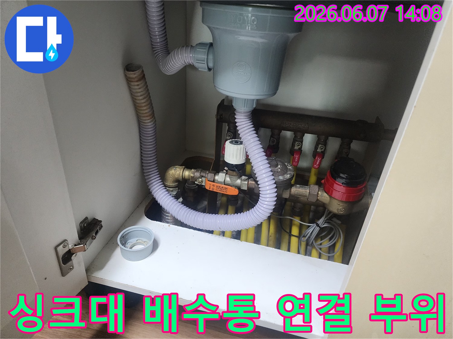 회색 주름관과 흰색 배수통이 연결된 싱크대 하부 모습