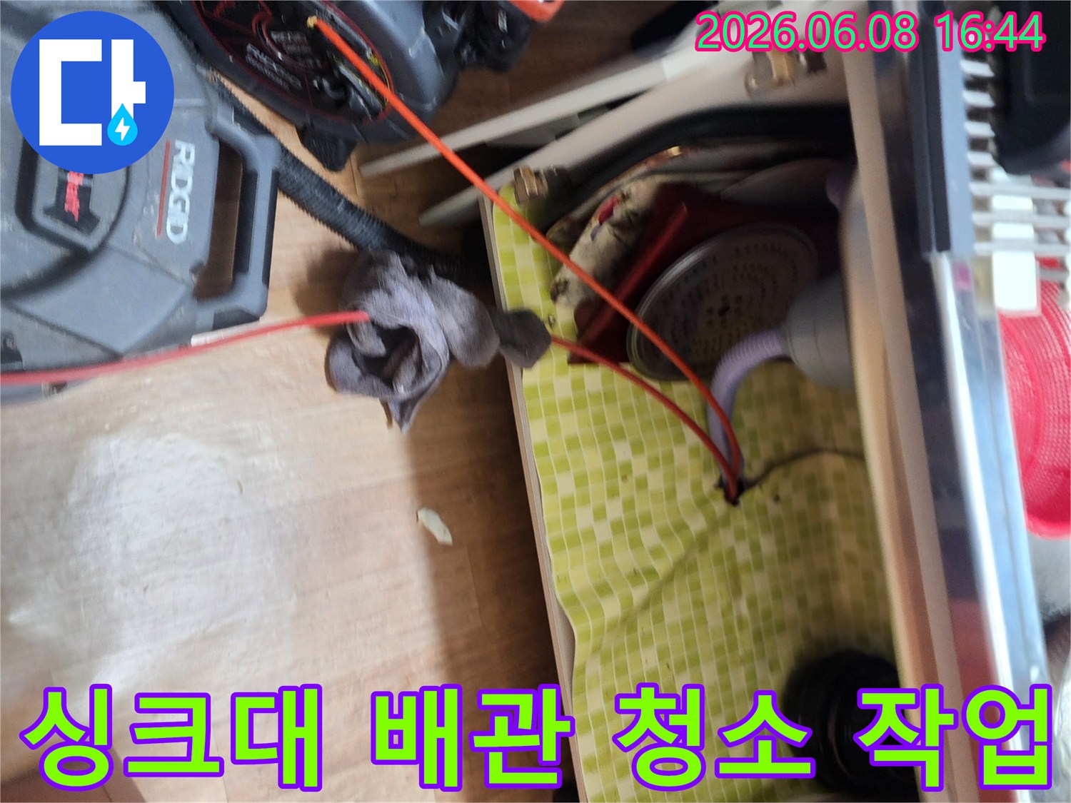 싱크대 하부장 아래 배관과 스케일링 장비가 놓인 현장입니다.