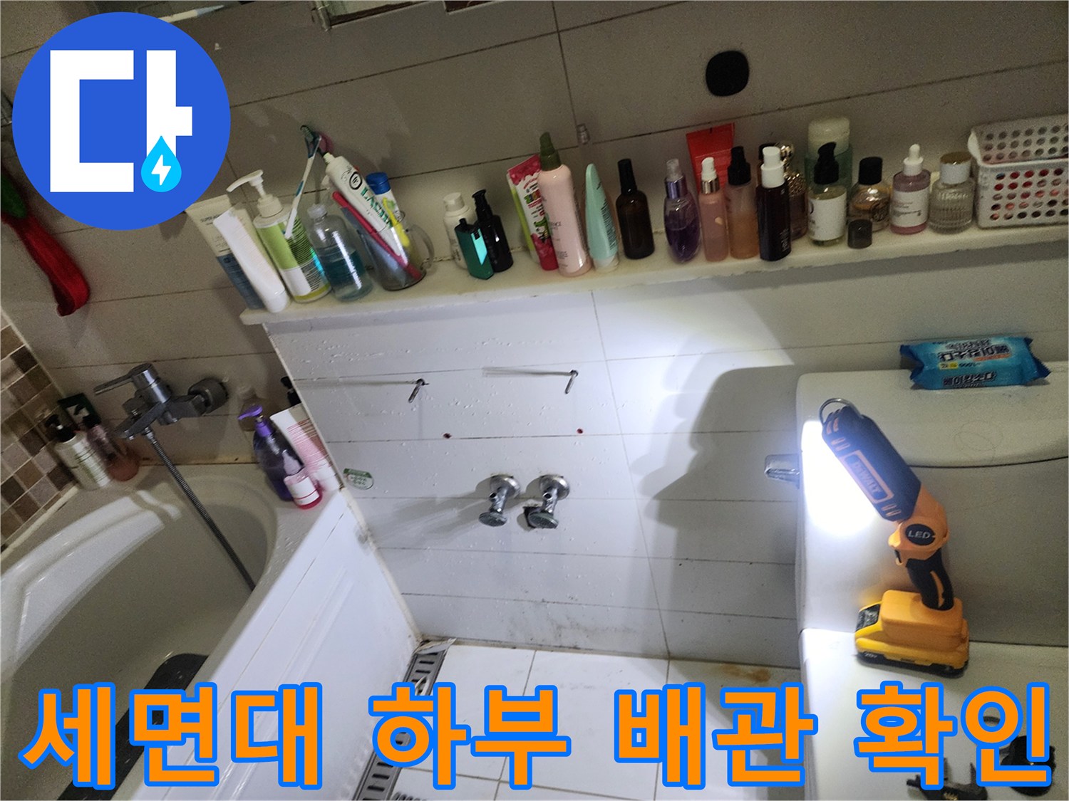 손전등 불빛으로 세면대 밑 좁은 공간의 누수 흔적을 찾는 장면
