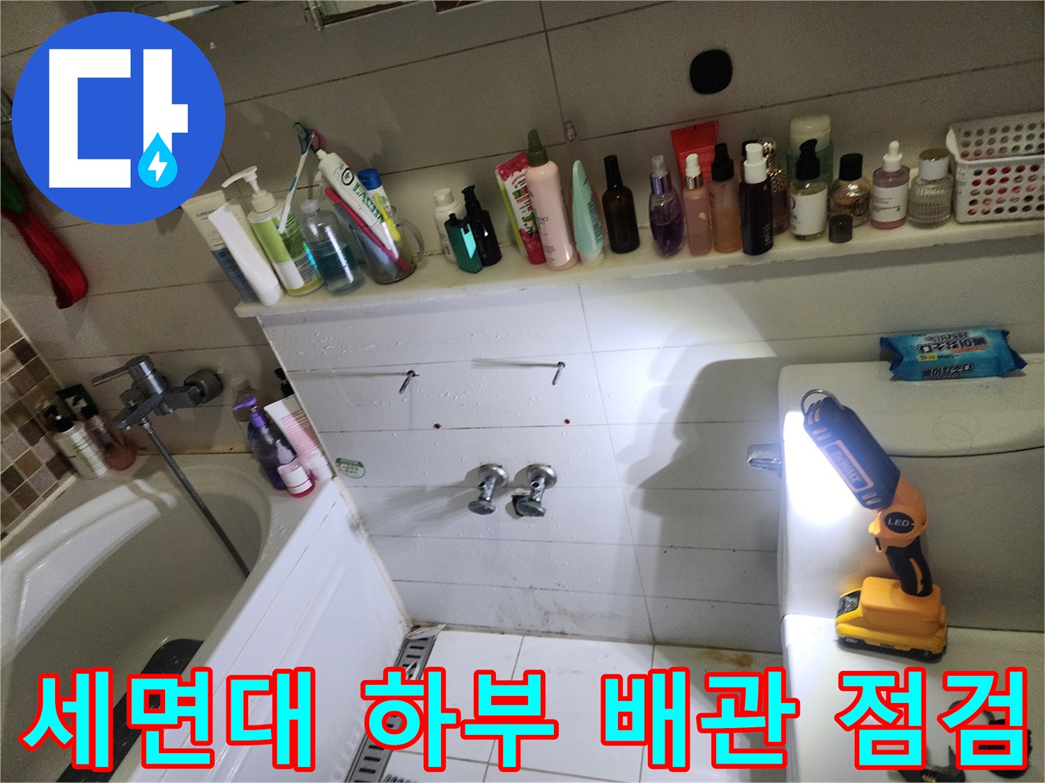 화장실 세면대 아래쪽 배관 연결 부위와 벽면 타일의 상태를 촬영한 사진입니다.