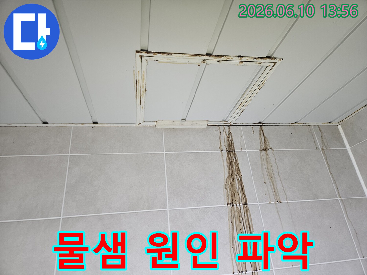 욕실 천장 점검구 주변에서 시작된 누수로-인해 타일 벽면이 오염된 모습을 보여줍니다.