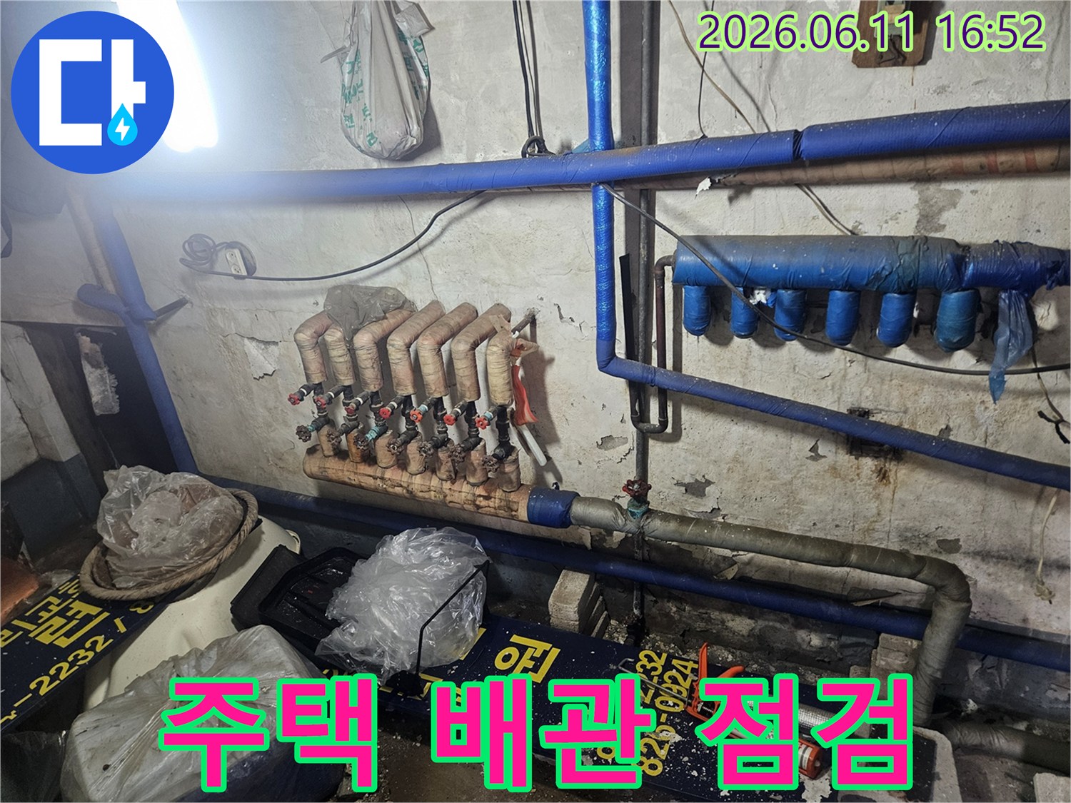 낡은 벽면을 배경으로-파란색과 갈색 단열재로 감싸인-다양한 크기의 배관들이 설치된 모습입니다.