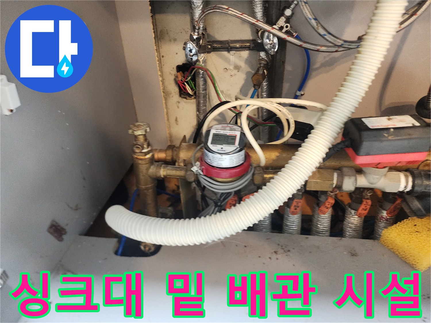 주방 싱크대 아래 설치된 금속 관과 흰색 주름 호스