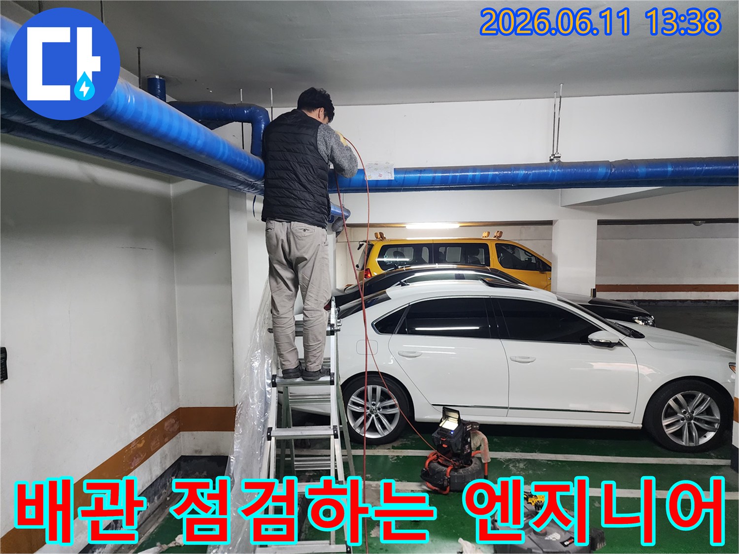 주차장 천장 파란색 배관을 살피며 사다리 위 작업 중인 기술자