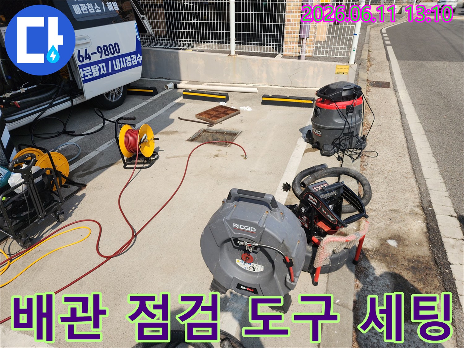 맨홀 주변에 놓인 노란색 호스 릴과 고압 세척용 리지드 장비 사진입니다.