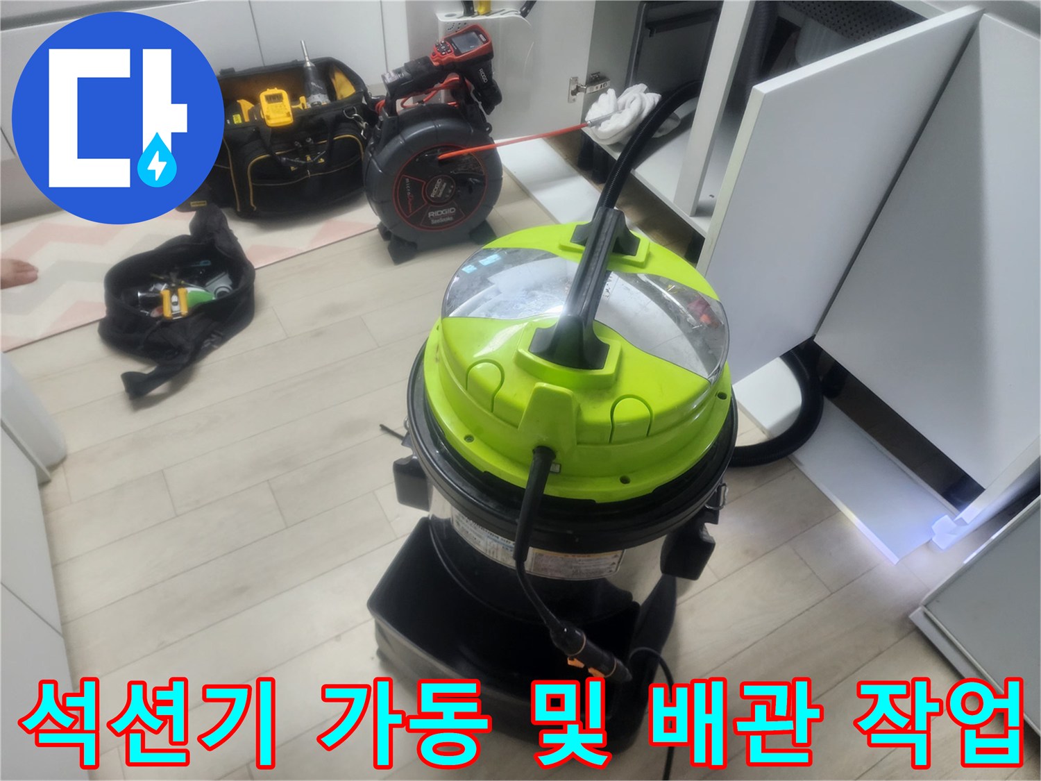 싱크대 밑 하부장 공간에서 석션기를 사용하여 배관 내부를 정밀하게 청소하는 모습입니다.