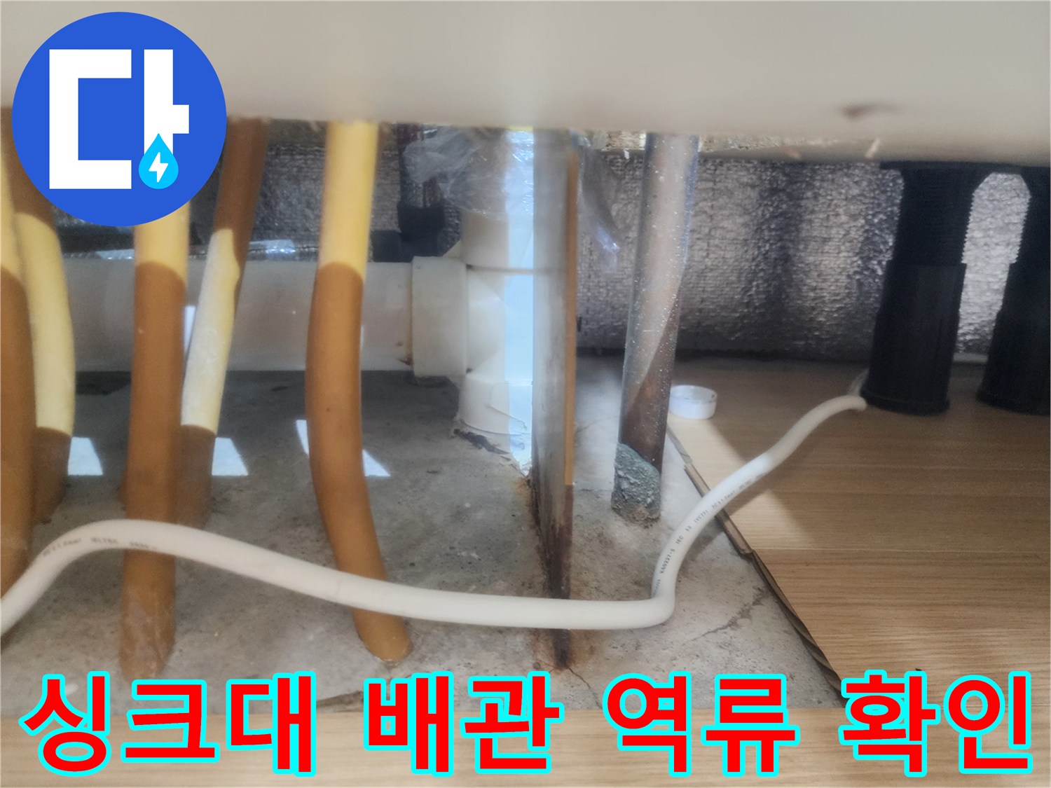 싱크대 하부장 내부 노란색 호스와 바닥 배수구 주변 근접 촬영
