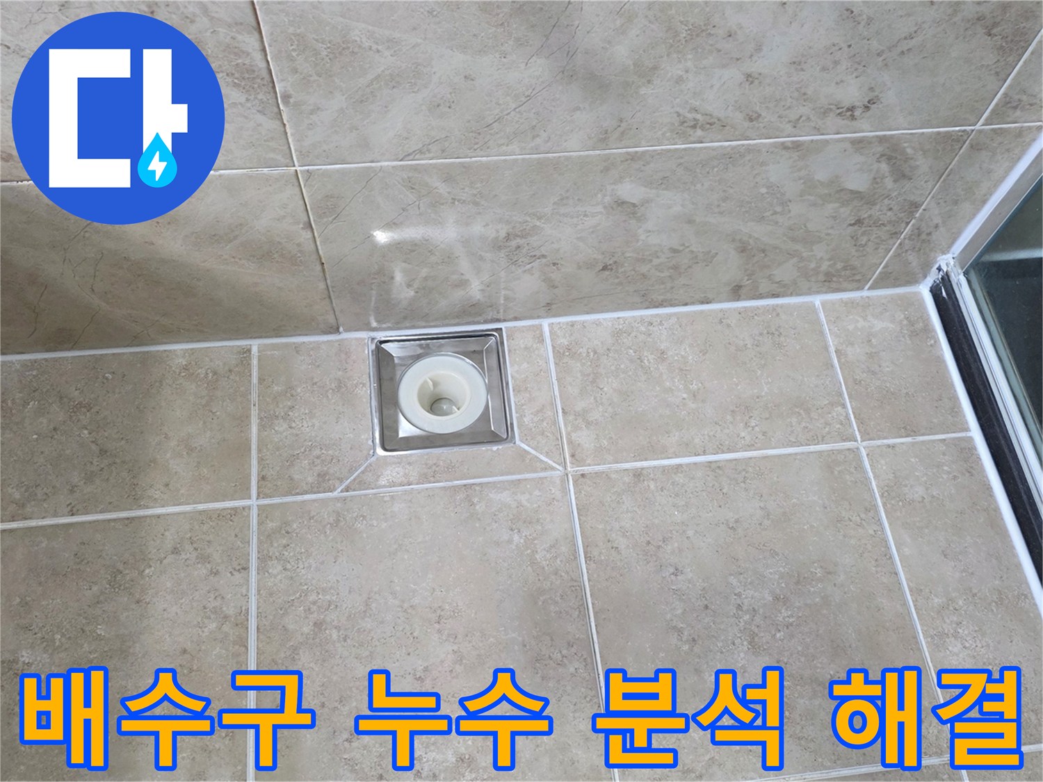 베이지색 타일 바닥에 설치된-사각형 금속 배수구의 모습으로-주변 타일과 줄눈의 상태를 면밀히 관찰하는 이미지입니다