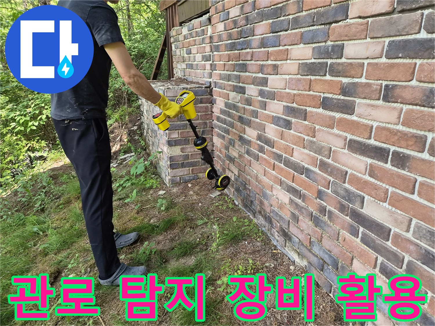 벽돌 건물 외벽 옆에서-관로 탐지기를 사용하여 땅속 매립된 배관 위치를 추적하는 모습입니다.