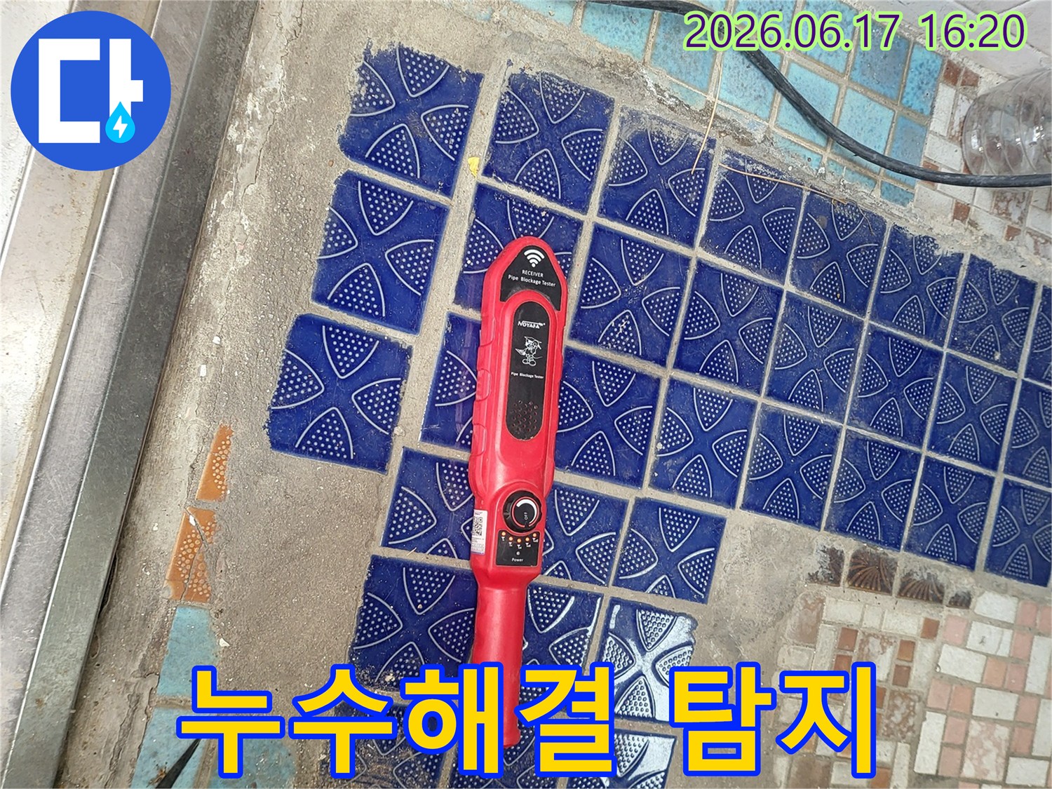 파란색 타일이 뜯겨나간 욕실 바닥에 놓인-붉은색 누수탐지 장비가-누수 해결을 위한 첫 단계인 탐지 작업 중인 모습
