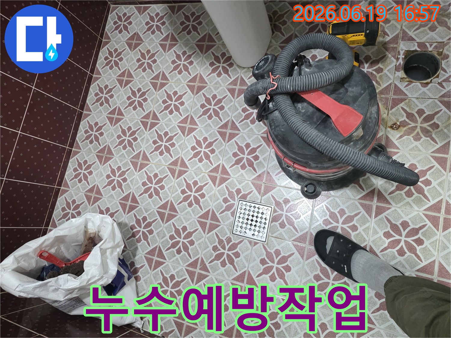 물기 제거를 위해 사용된-산업용 습식 청소기가-욕실 바닥에 놓여 있고-배수구와-작업자의 발이 함께 보이는 장면
