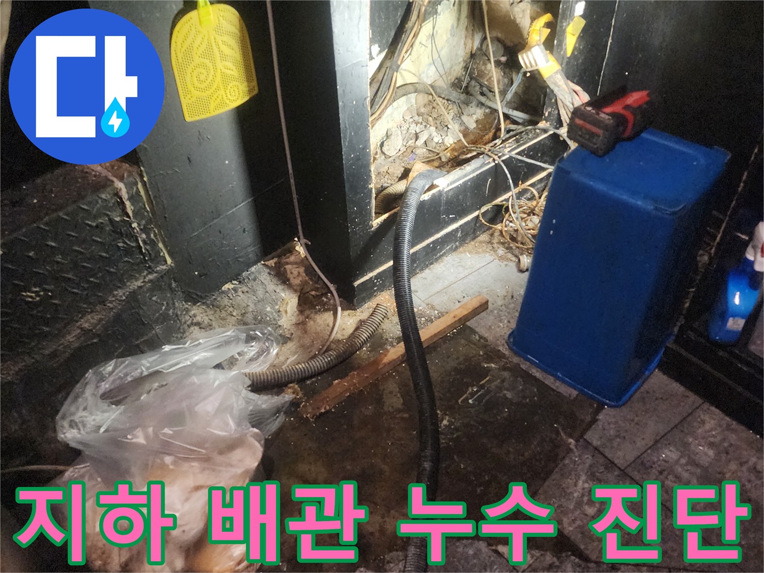 어두운 상가 바닥 아래에서 복잡하게 얽힌 배관과 전선-그리고 물이 새는 흔적을 보여주며 지하 배관 누수를 정밀 진단하는 현장 이미지