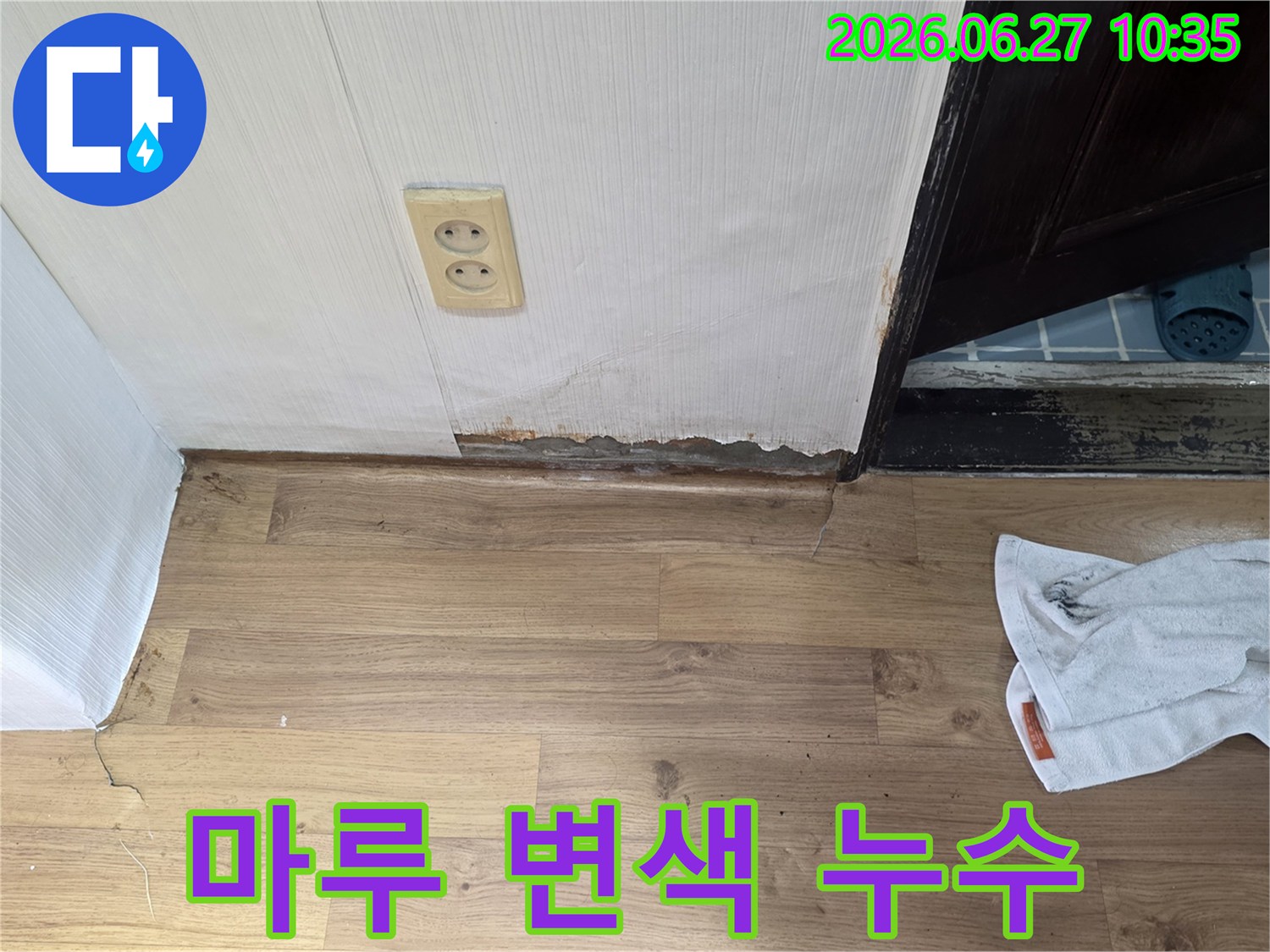 벽면 하단과 마루 경계 부분에 물기가 스며들어-변색되고 손상된 누수 현장의 모습입니다.