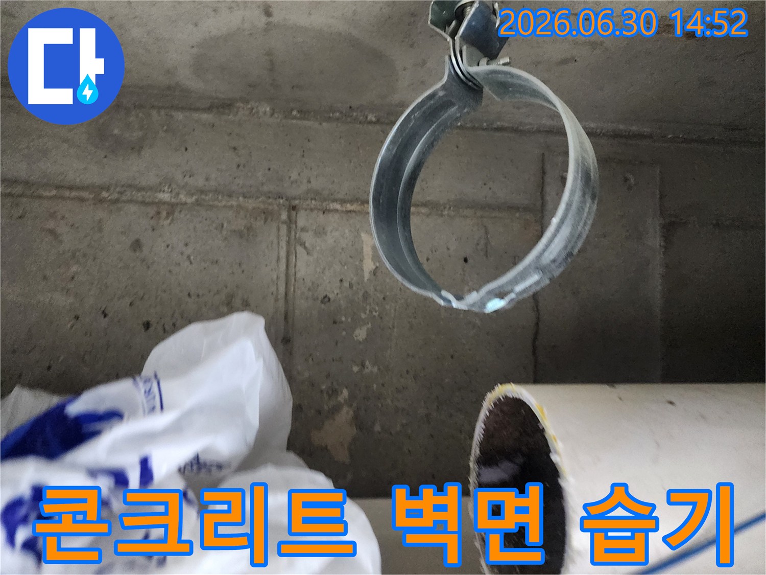 습기가 스며든-콘크리트 벽면과-배관 고정 밴드가 보이는-누수 현장 클로즈업