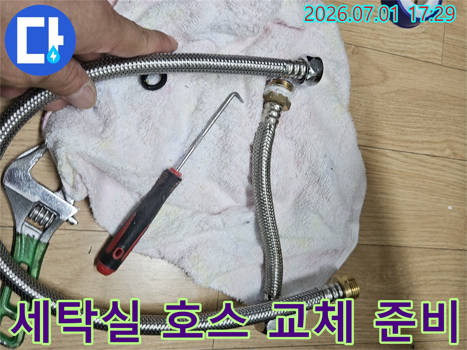 이 이미지는 아파트 베란다 세탁실 수도 호스 교체를 위한-새로운 호스와 작업 도구를 보여주는 현장 사진입니다