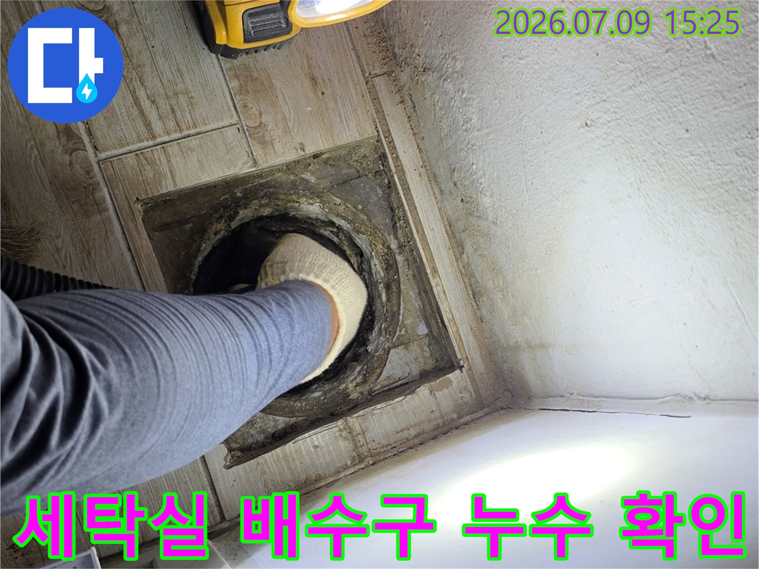 손전등으로 비춘 세탁실 바닥 배수 트랩과 파손된 주변부