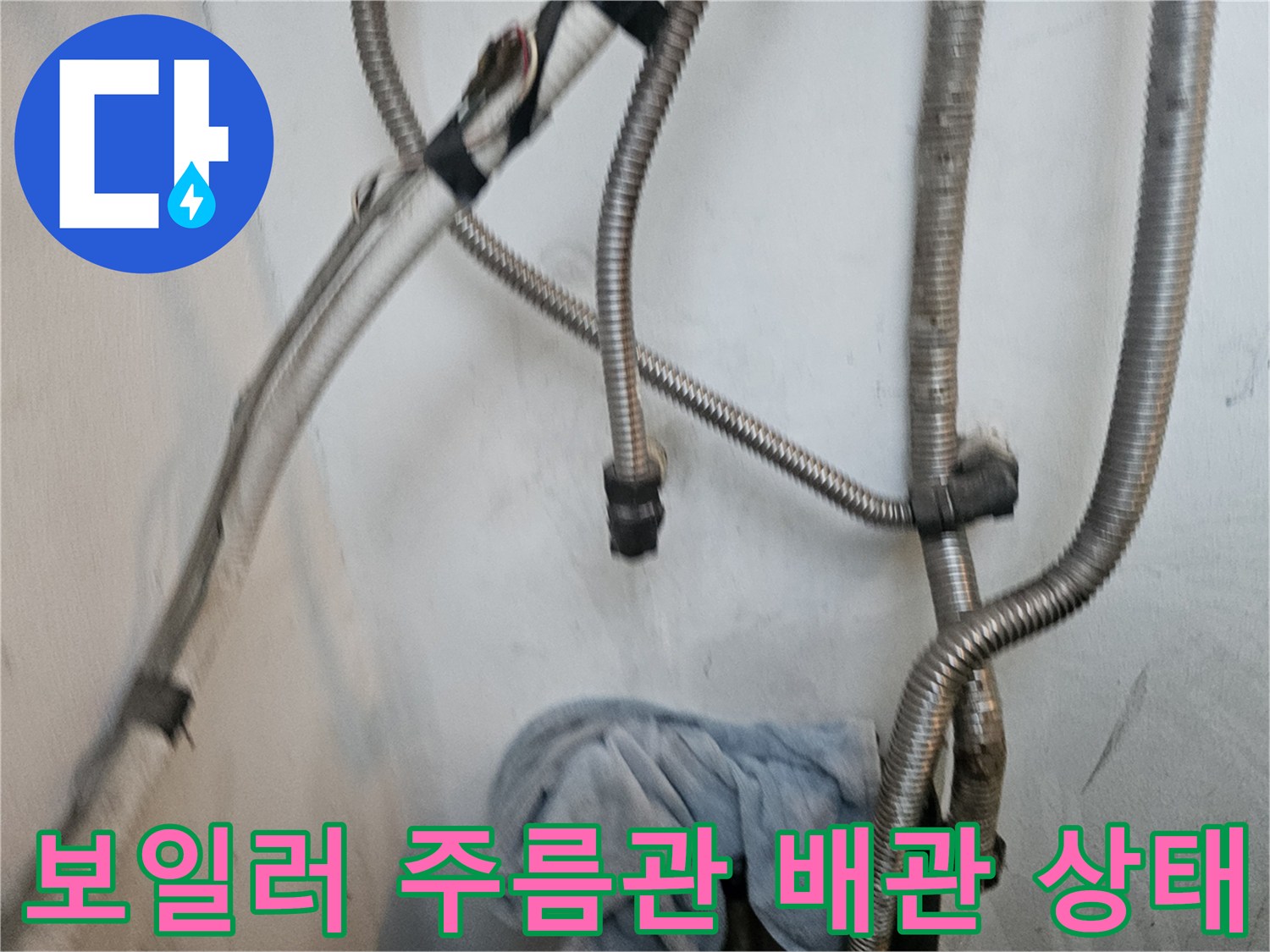 보일러 하단부에 연결된 금속 재질의 주름관과 배관 연결 부위 모습입니다.