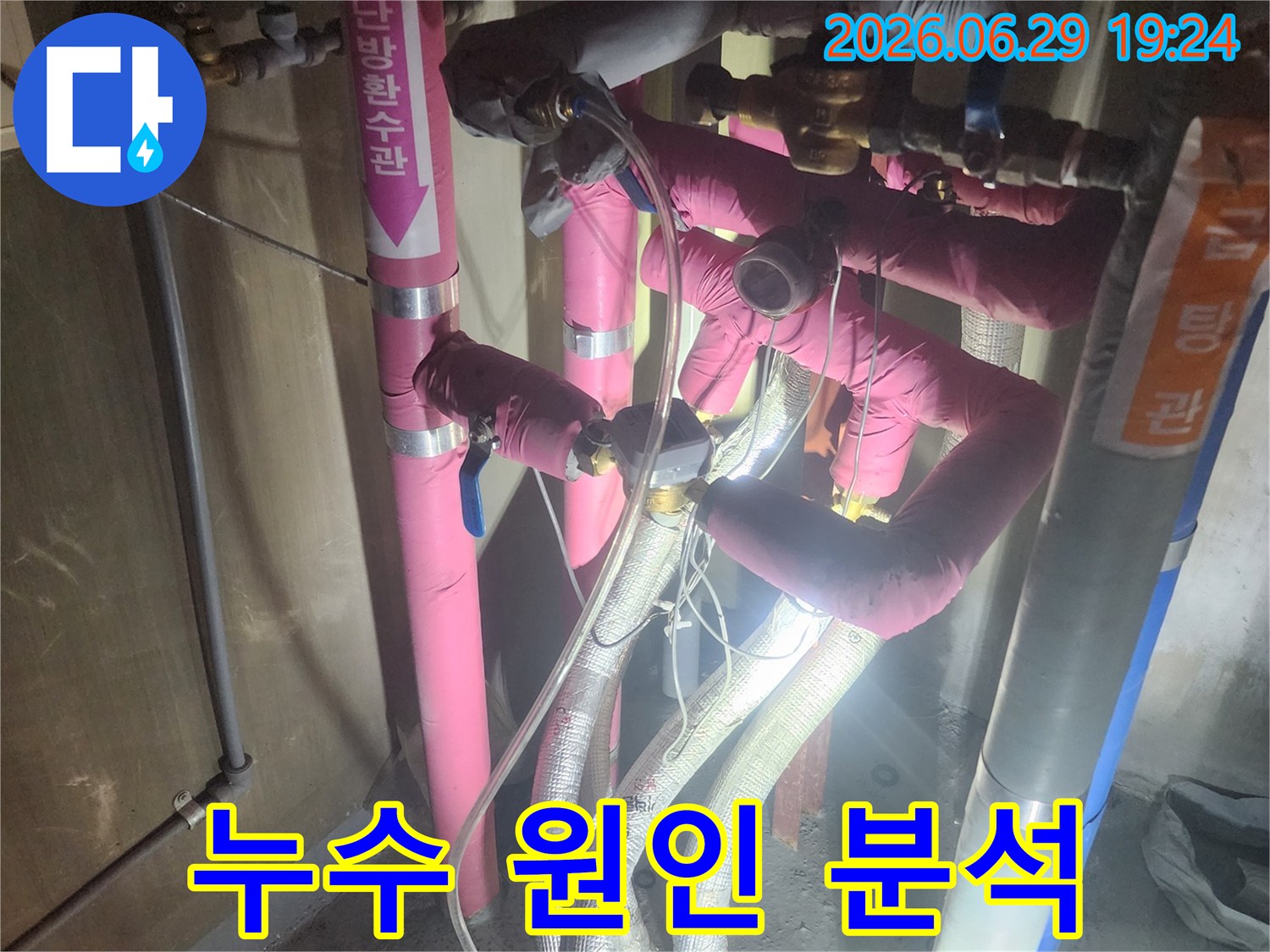 분홍색과 회색 단열재로 덮인-배관들이 복잡하게 얽혀있고-압력 게이지가 연결된-누수 테스트 현장입니다