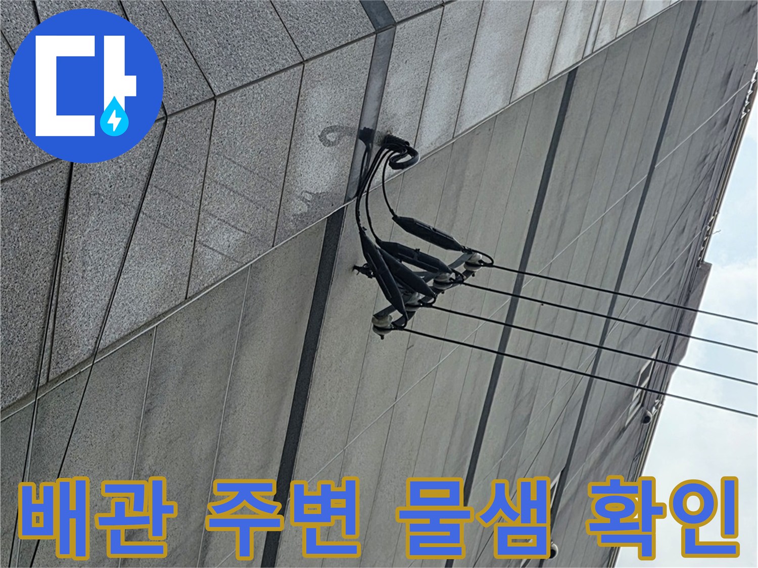아파트 외벽에 설치된 배관의 연결 상태와 벽면 접촉부를 점검하는 모습입니다.