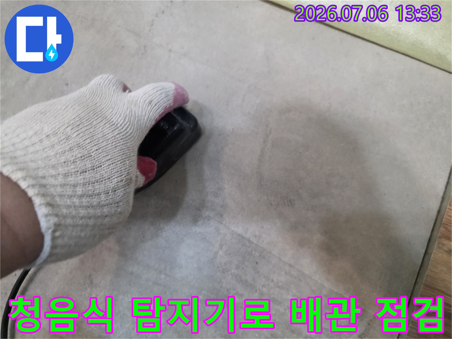 장갑을 낀 손으로 청음식 탐지기를 사용하여 바닥 아래 매립된 배관의 누수 지점을 정밀하게 확인하는 모습