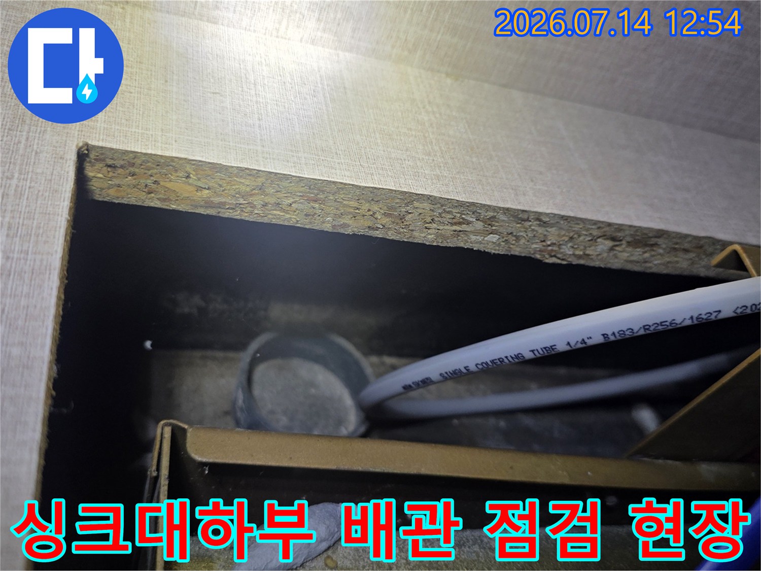 싱크대 하부 공간에 노출된 흰색 급수 배관과 연결 부위를 점검하는 모습