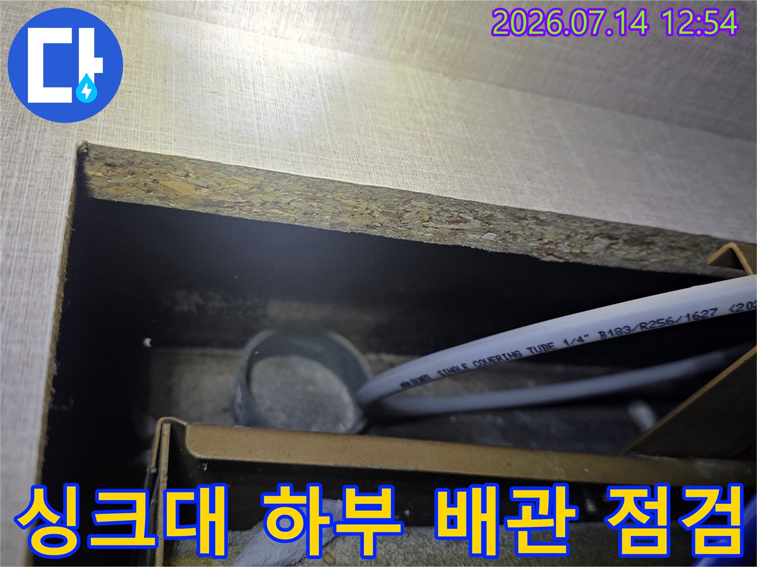 싱크대 하부 공간에서 노출된 급수 및 온수 배관을 정밀하게 점검하는 모습