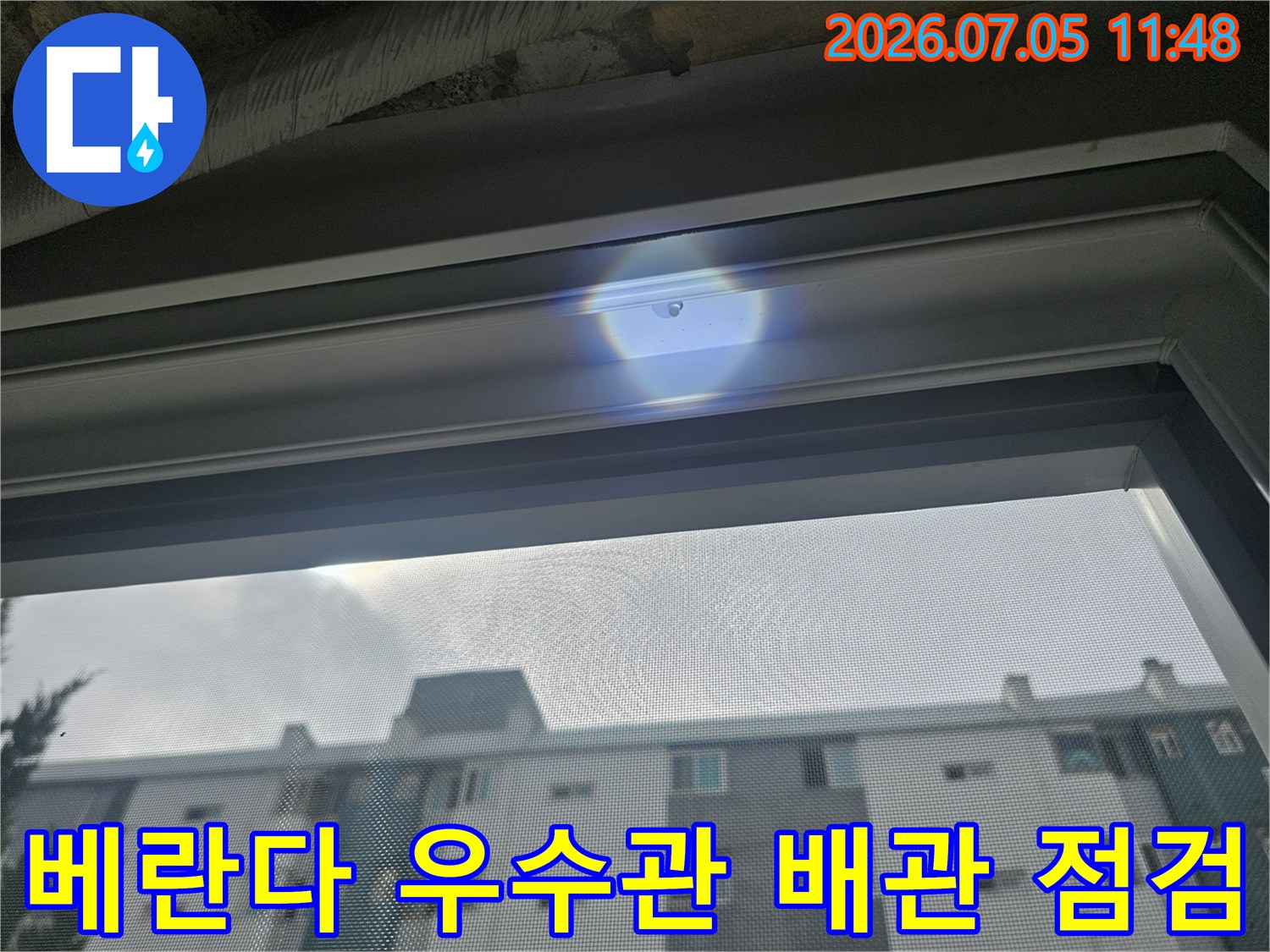 베란다 창문 너머로 보이는 아파트 단지와 연결된 우수관 부위의 누수 정밀 진단 모습
