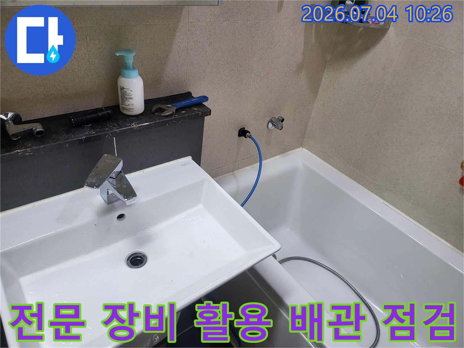 세면대 주변 배관에 연결된 파란색 호스와 압력측정기가 있는 누수 점검 현장