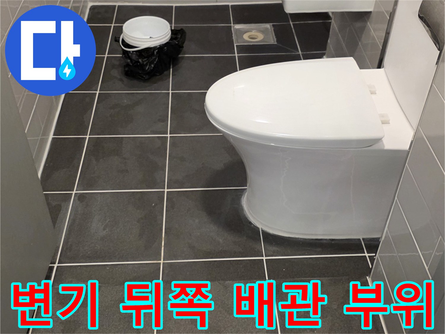 변기 뒷부분의 어두운 색 타일과 배관 연결부 사진입니다.