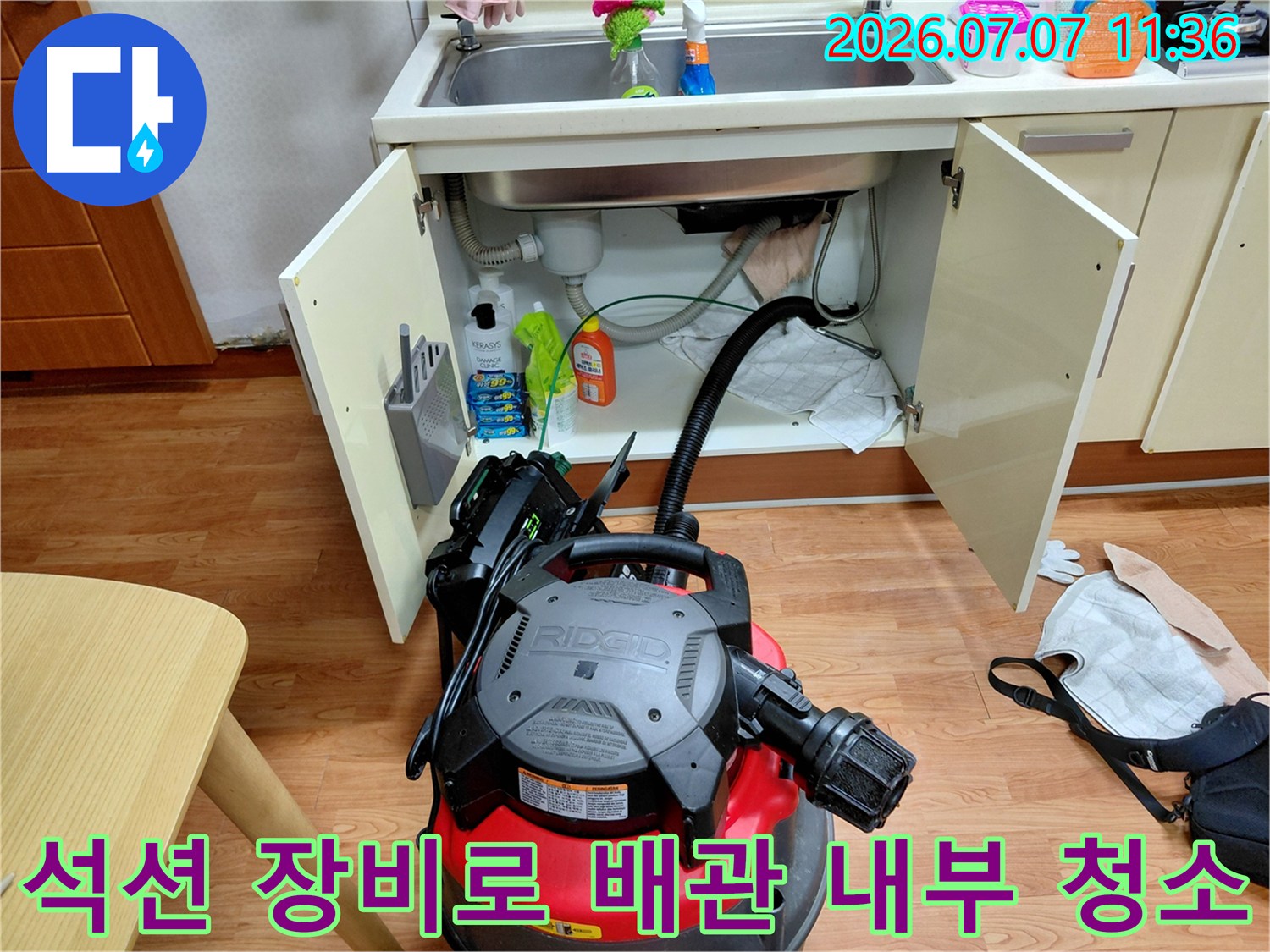 빨간색 석션 기계가 싱크대 하단부 배관에 연결되어 오물을 제거하는 모습