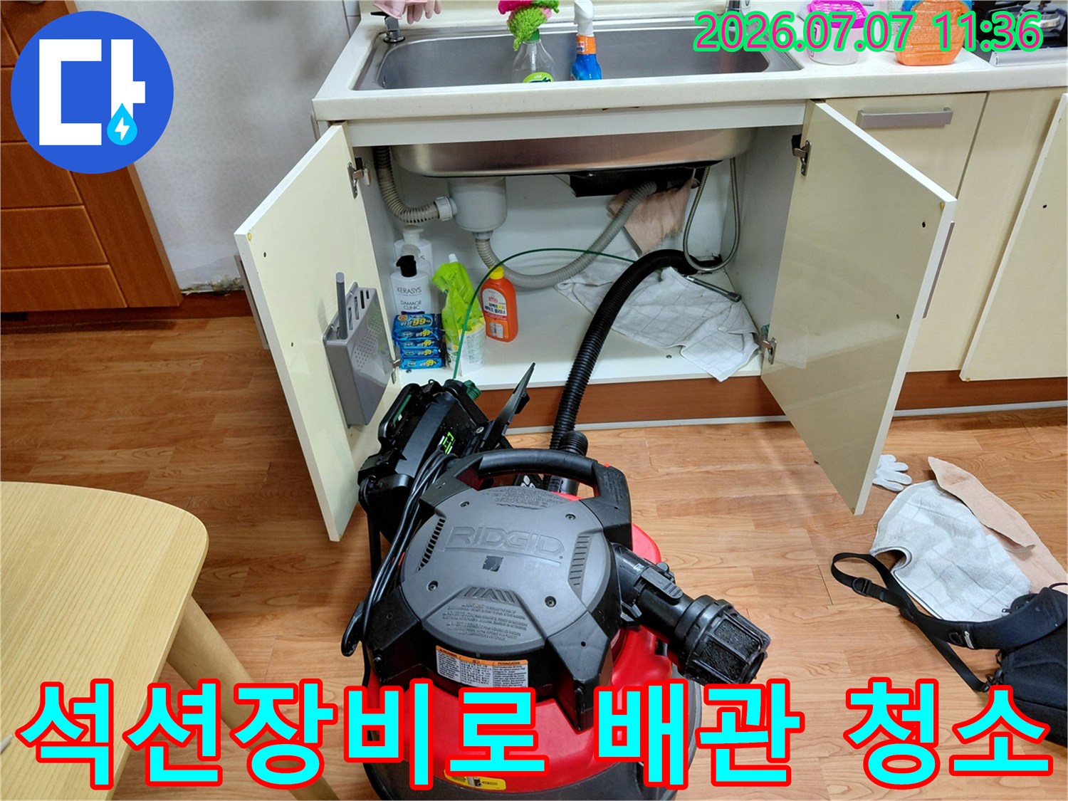 싱크대 하부장에서 석션 장비를 사용하여 배관 속 오물을 흡입하는 장면