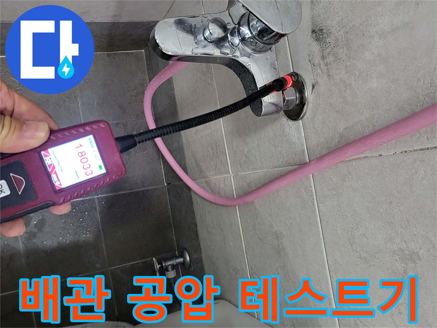 수전 근처 배관에 연결된-디지털 압력계와 분홍색 호스 모습입니다.