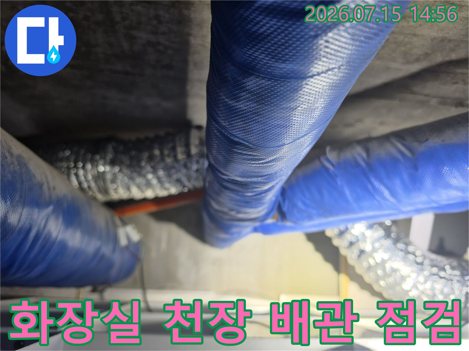 파란색 보온재로 감싸진 화장실 천장 배관과 은색 단열재가 있는 내부 모습