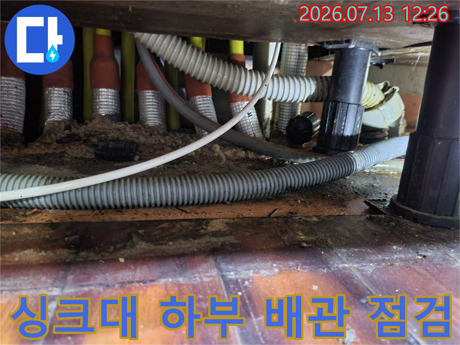 싱크대 아래 노출된 여러 개의 배관과 연결 부위를 정밀하게 점검하는 모습