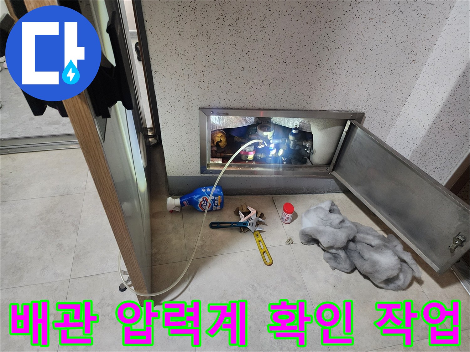 점검구 안쪽 배관에 연결된 파란색 호스와 압력 측정 장비의 모습입니다.